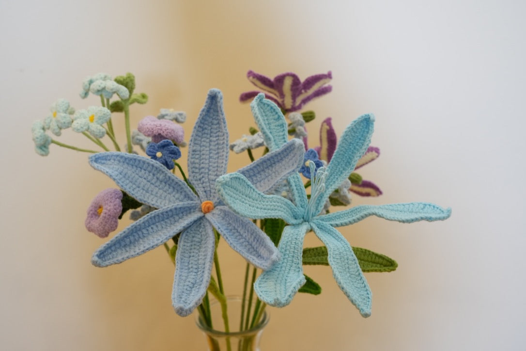 Handmade blue and turquoise crochet lilies with pastel flowers in a glass vase