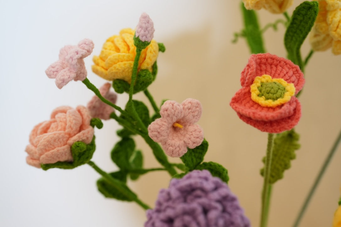 Close-up of handmade pink, yellow, coral and purple crochet flowers with green stems