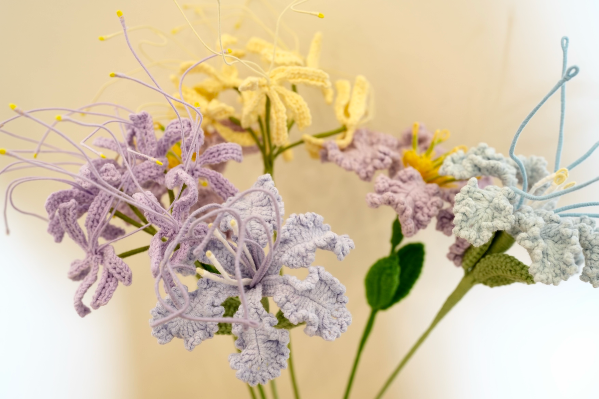 Close-up of lavender, pale yellow and light blue handmade crochet lilies against a cream background